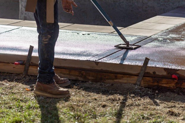 Concrete contractor applying release agent and finishing stamped concrete surface during installation