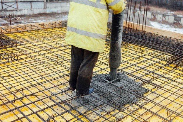 Concrete contractor pouring wet concrete into reinforced rebar grid for slab foundation installation
