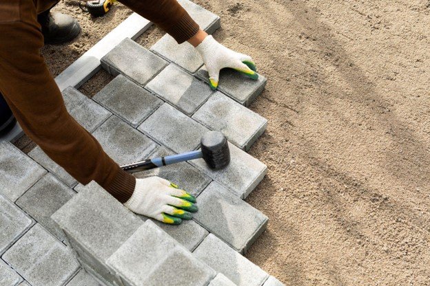 Contractor installing concrete pavers with rubber mallet during driveway installation process